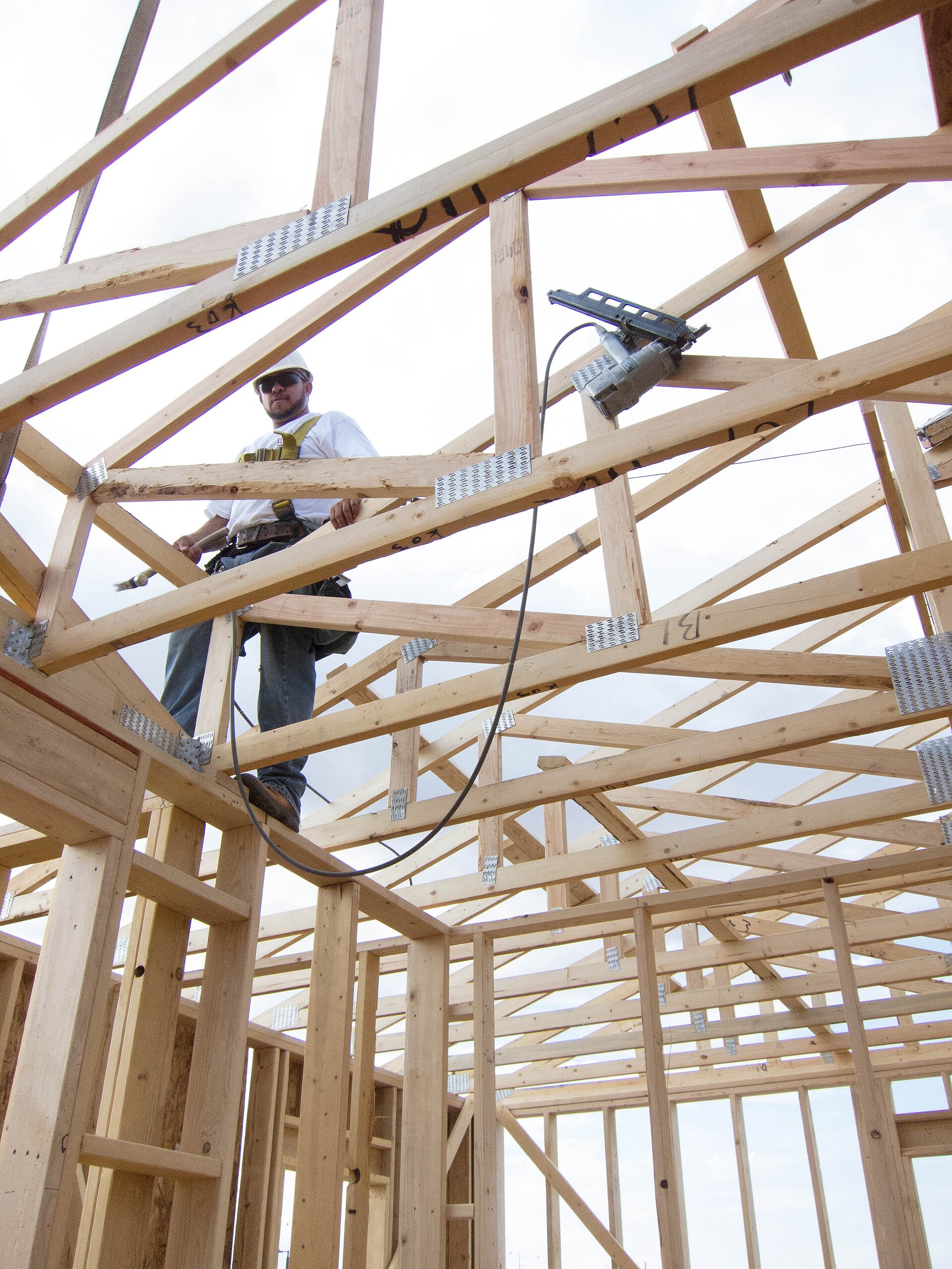 A carpenter wearing a hard hat and harness on a timber house frame